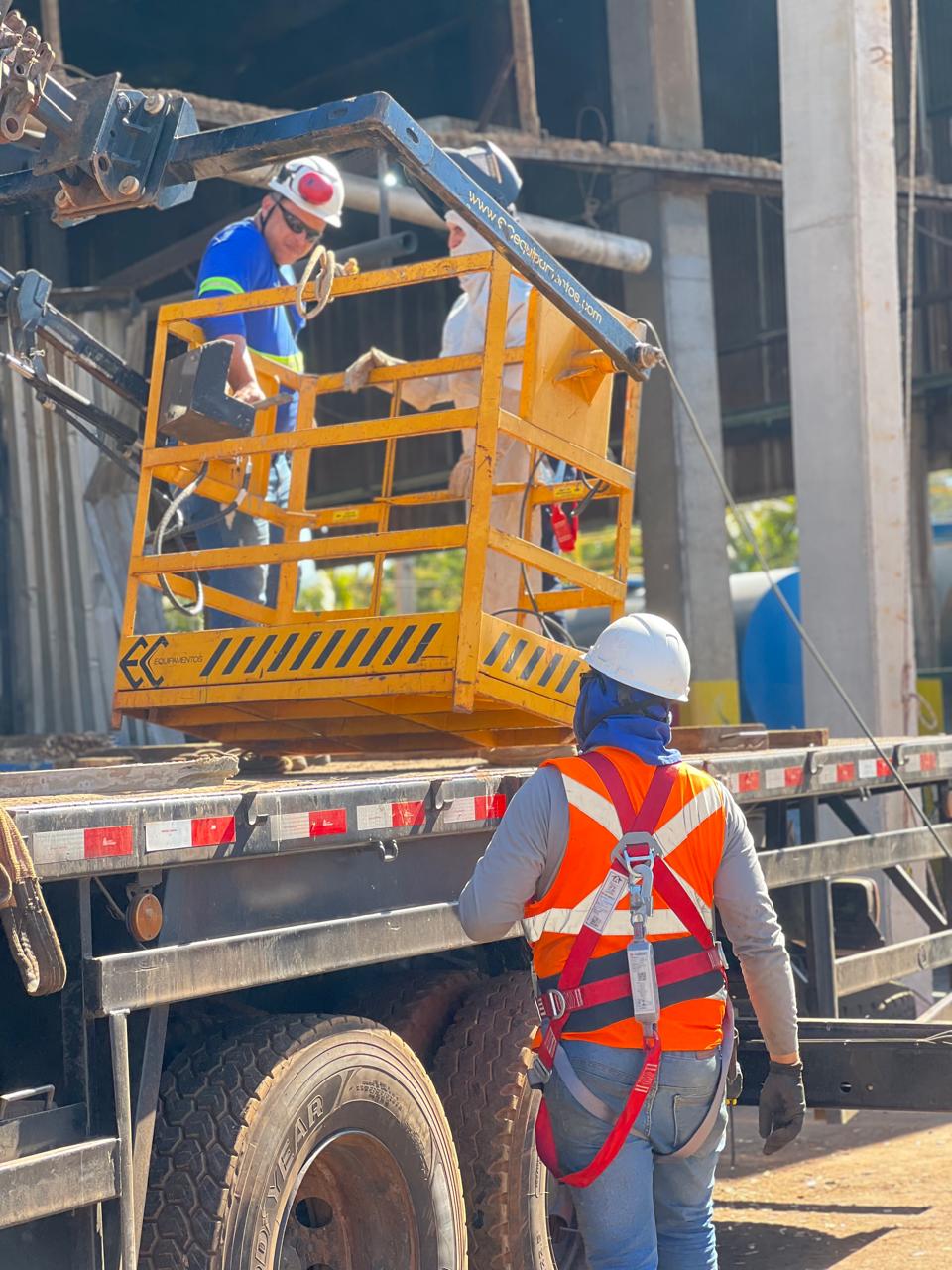 Equipe de montagem com EPIs completos operando plataforma sobre caminhão